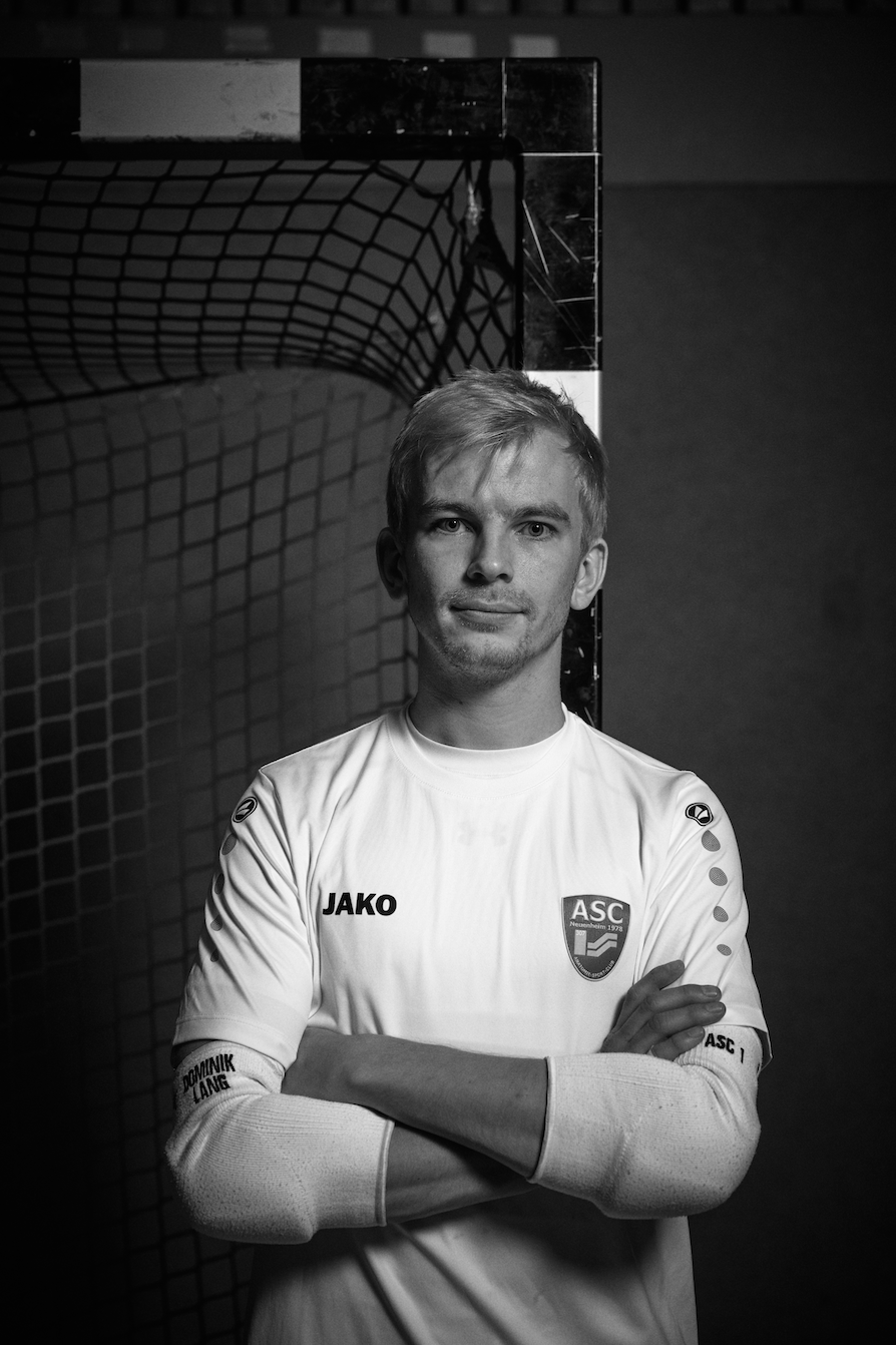 Dominik Lang. Futsal Torwart in Heidelberg beim ASC Neuenheim. Verschränkte Arme angelehnt an Torpfosten, schwarz weiß.